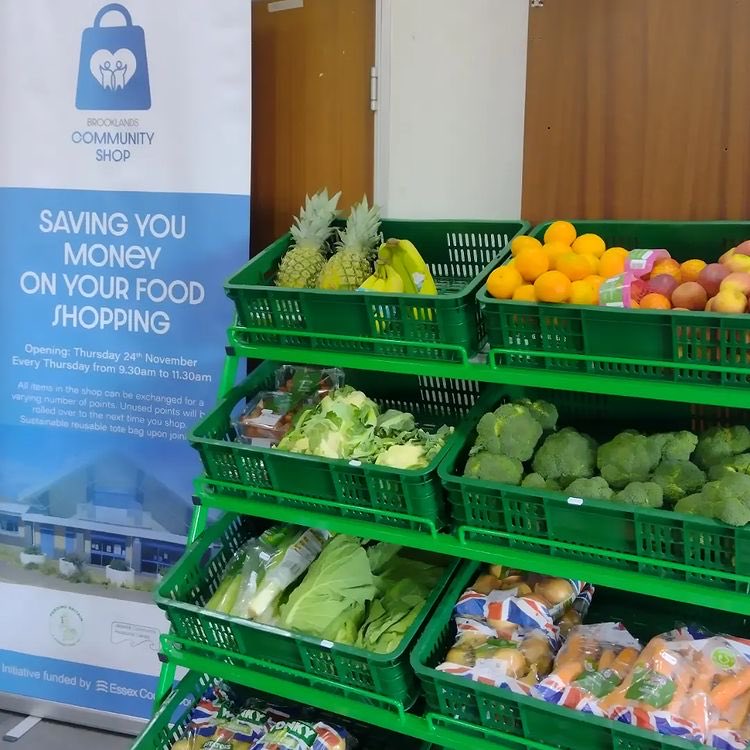 A photo of a stack of green crates filled with fresh fruit and veg beside a blue sign for the affordable food club