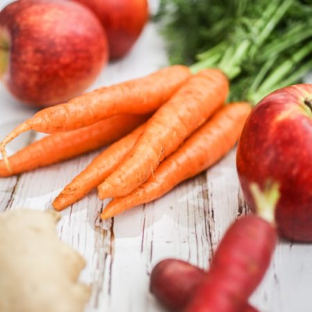 A photo of some vegetables and fruit on a table including carrots, apples, radishes